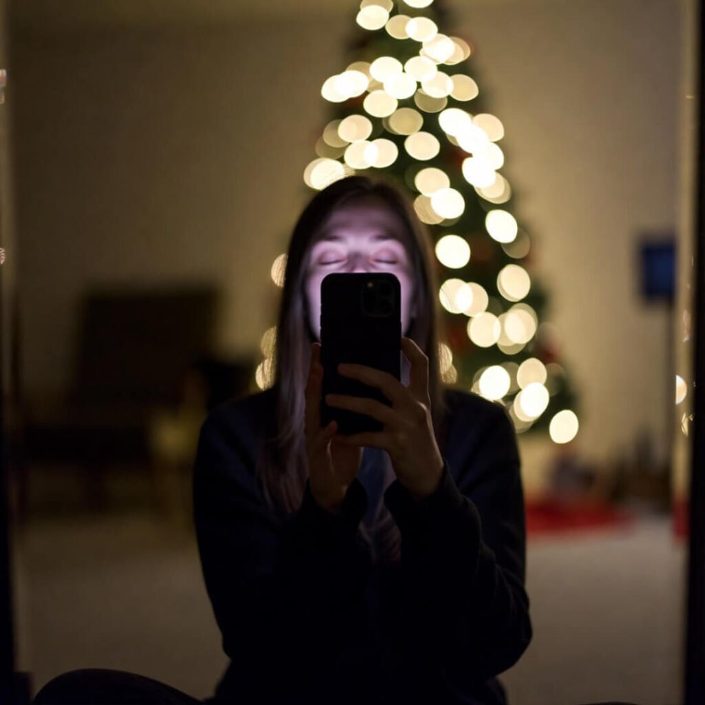 Blurry mirror selfie with eyes closed, Christmas lights behind.