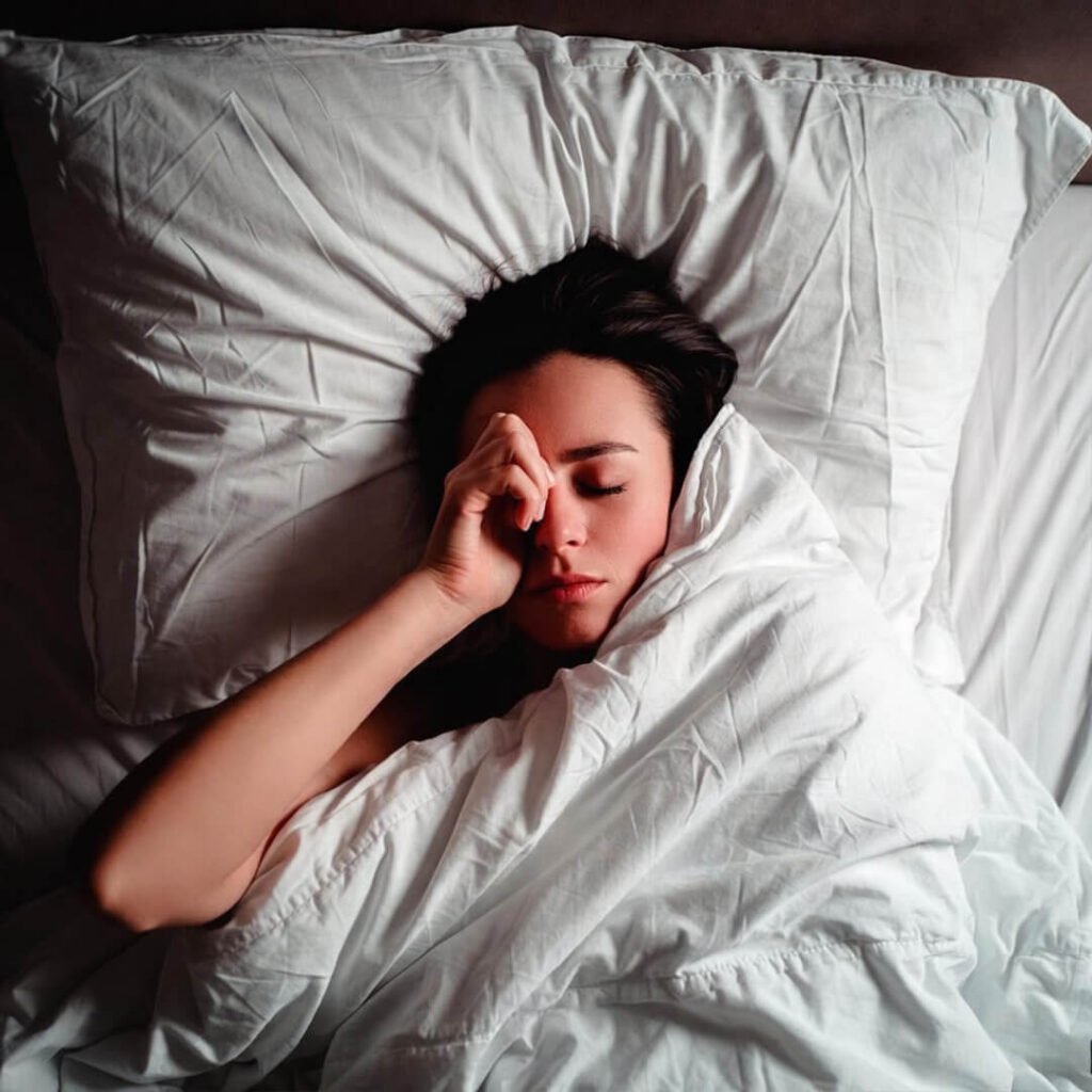 Person rubbing eyes in tangled bed sheets.