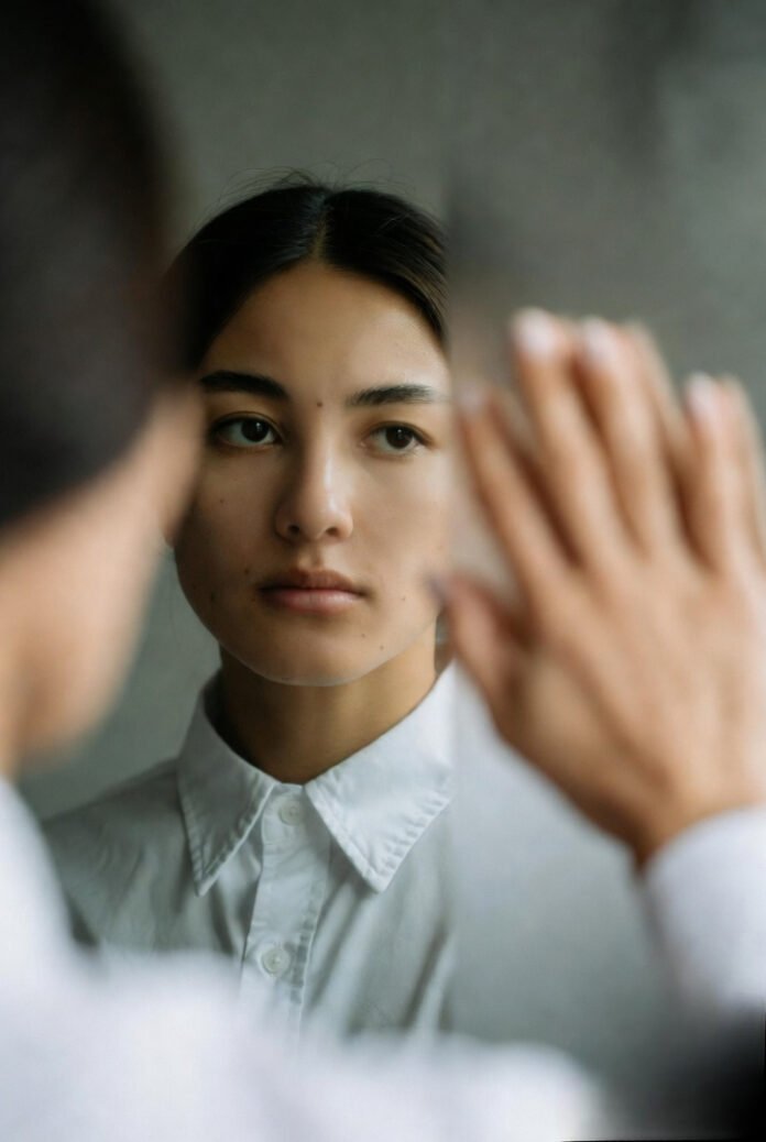 A person looking at their reflection in a slightly foggy mirror, hand touching the glass