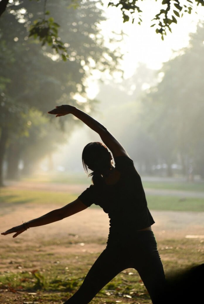 someone stretching outdoors in a quiet park, trees softly swaying, peaceful but not overly staged.