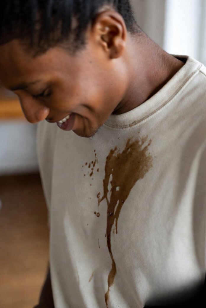 A candid moment of someone looking down at a coffee spill on their shirt but smiling or shrugging it off.